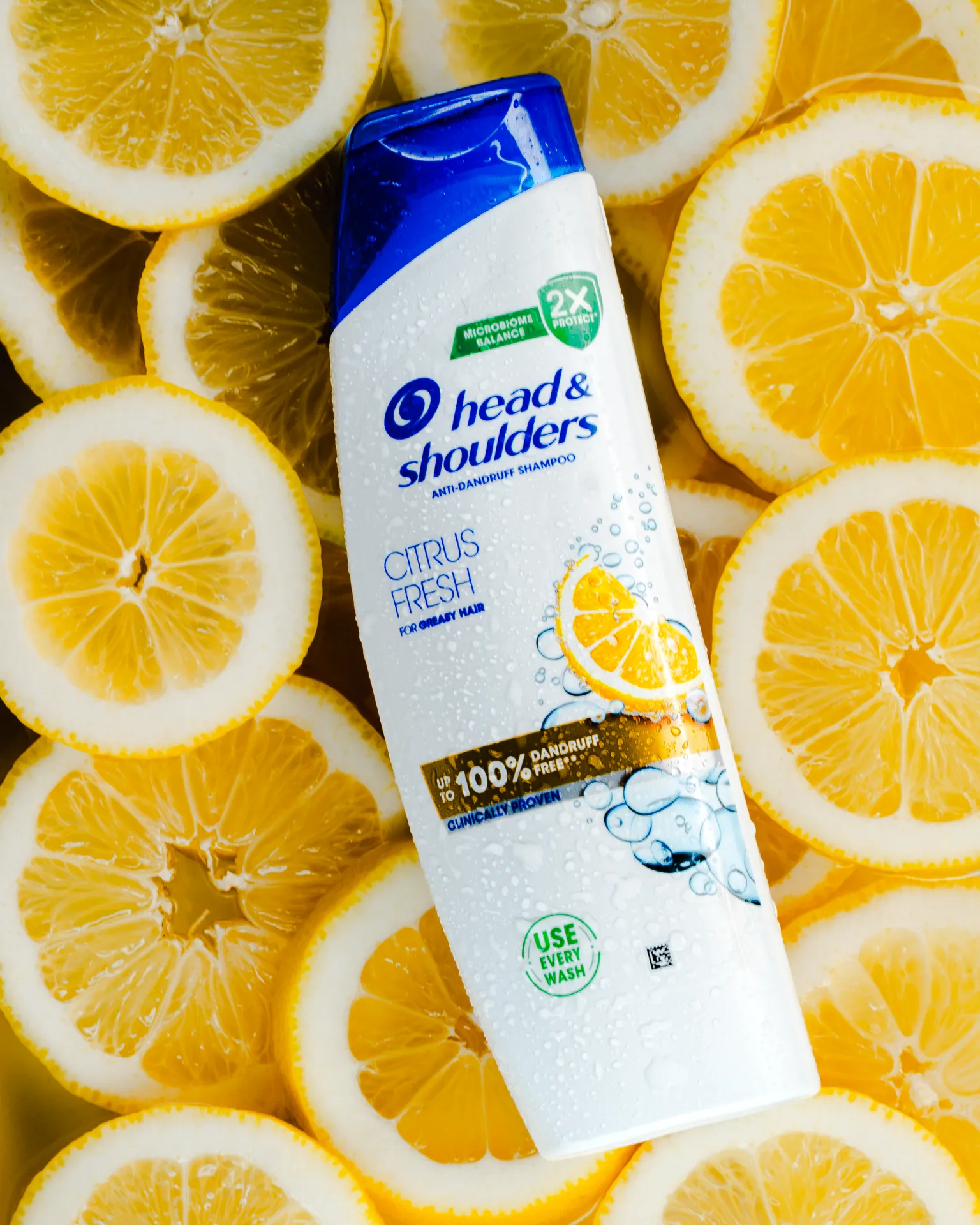Head & Shoulders - Citrus Fresh — A bottle of Head & Shoulders Citrus Fresh anti-dandruff shampoo sits among sliced lemons, with water droplets on the packaging suggesting freshness in a commercial product shot.